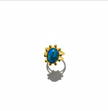 Bague Majoa Azura ajustable en acier inoxydable doré avec une pierre bleue ovale sertie de perles métalliques.