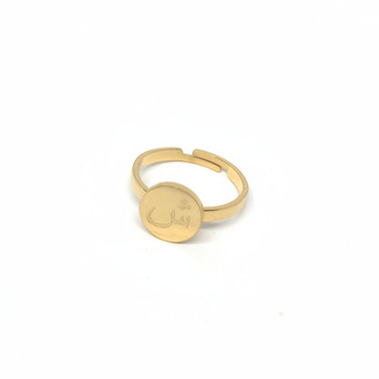 Majoa gold stainless steel ring with Arabic letter engraving on a round medallion. Minimalist design.