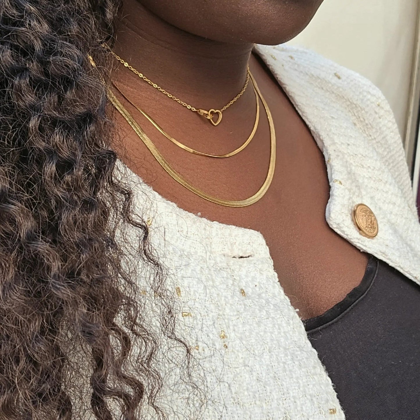 Majoa gold layered necklaces with heart pendant, worn by a woman with dark skin and curly hair.