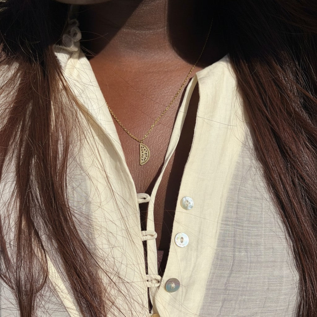 Majoa gold watermelon slice pendant necklace on a woman wearing a cream-colored button-up shirt.
